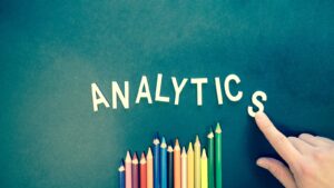 Crayons de couleur et lettres orthographiant « ANALYTICS » sur un fond texturé avec une main.