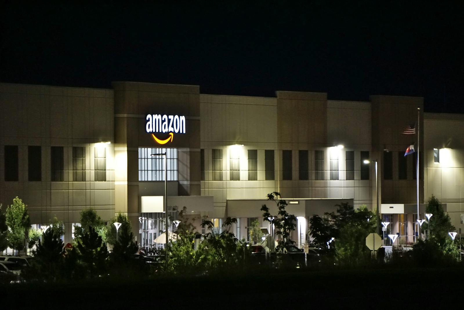 Entrepôt d'Amazon illuminé la nuit avec des arbres et une signalisation.